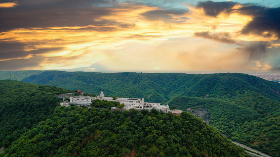 aerial drone shot flying towards the famous landmark chulgiri jain temple on agra jaipur road after ghat ki guni tunnel, white building perched atop lush green aravalli hill mountains