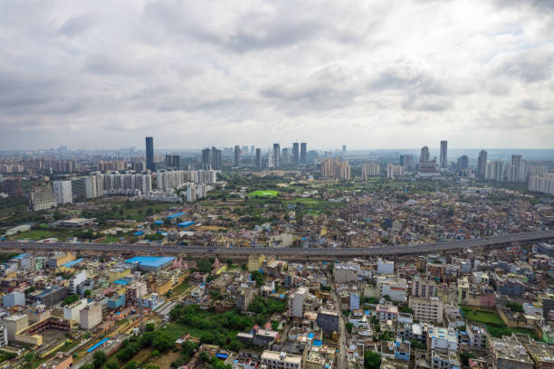 aerial drone shot over gurgaon showing monsoon clouds with light rays falling on ground crowded with homes houses, sohna highway feilds and water pools around under construction buildings