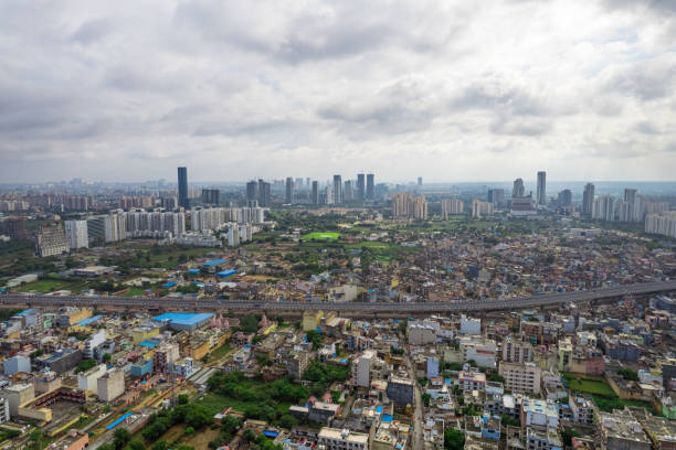 aerial drone shot over gurgaon showing monsoon clouds with light rays falling on ground crowded with homes houses, sohna highway feilds and water pools around under construction buildings stock photo
