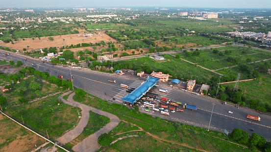 Aerial drone shot showing congestion traffic at toll booth on national highway in India with cars, trucks and vehicles waiting to cross the blue roofed structure with green trees all around. Expedited by cashless Fastag payment