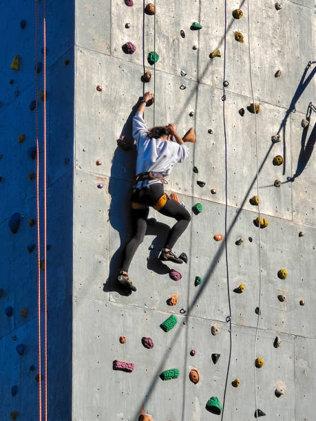 アスリートの女の子が多くのフックでクライミング用のトレーニングウォールを登ります。下からの眺め - climbing mountain climbing rock climbing women ストックフォトと画像