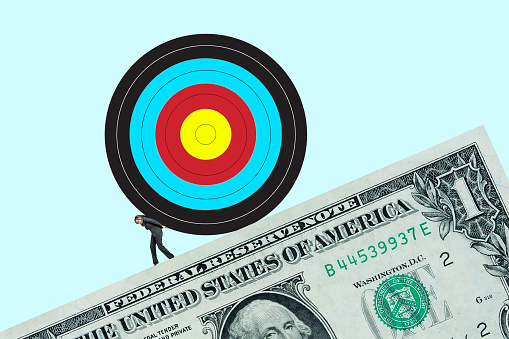 A woman pushes a large target up a slope created by a one dollar bill isolated against a light blue background.