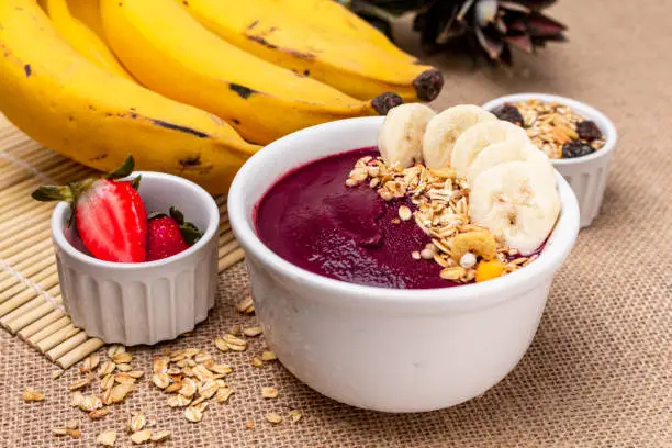 Acai bowl on the table with jute canvas, with berries and oat flakes, front view. Brazilian popular food.