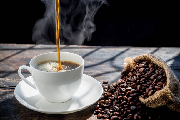 istock The steam from Pouring coffee into cup , A cup of fresh coffee on old kitchen table. with copy space. A scattering of coffee beans with a cup of coffee. Coarse fabric.hot food and healthy meal concept 1454094630