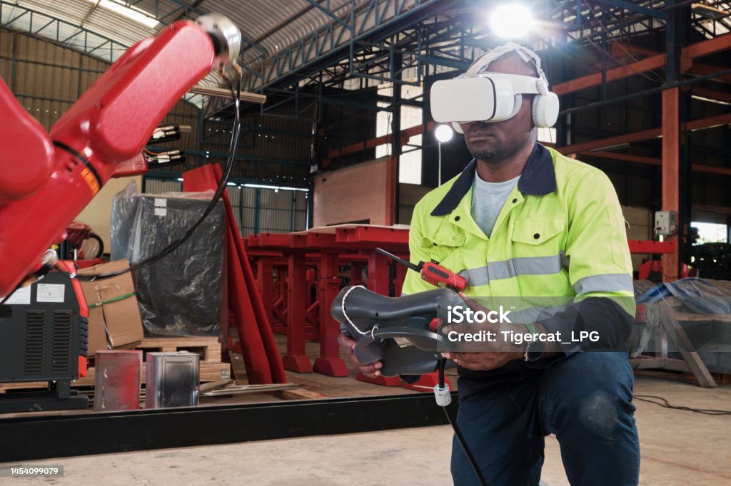 Black engineer with VR glasses controls robotic arm in manufacturing factory. An African American engineer with VR glasses controls robotic arm, virtual simulator software in mechanical manufacturing factory, and intelligent automatic machines technology in industry innovation. Virtual Reality Simulator Stock Photo