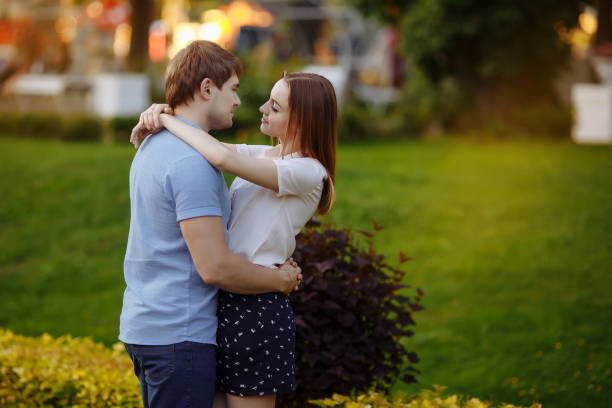 Happy young couple in love in summer casual clothes walking in the park. Man and woman eat cotton candy and have fun outdoors.