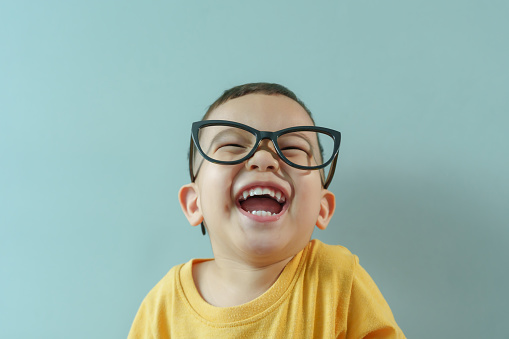 Portrait of Cheerful little Asian boy in yellow shirt and eyeglasses laughing on blue isolated background. Carefree, Joyful, Smiling face, Elementary school student, Back to school