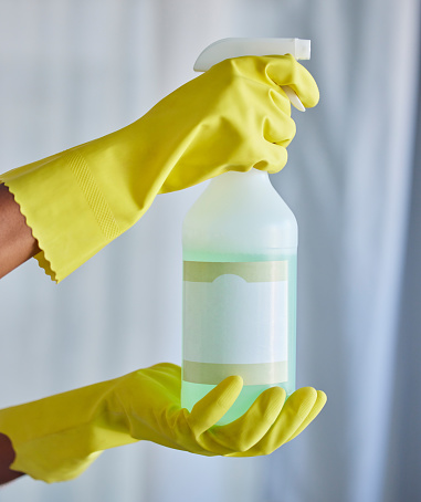 One unrecognizable woman holding a cleaning product while cleaning her apartment. An unknown domestic cleaner wearing latex cleaning gloves and holding and unlabelled organic cleaning agent