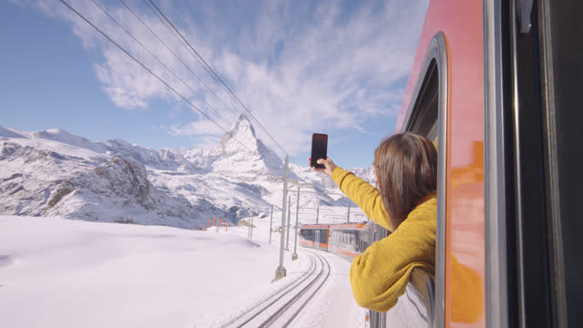 Excitment of female taking photos with her smartphone at from out window traveling by train to travel at matterhorn mountain, Zermatt in Switzerland, Europe.Experiential travel with diversity concept.With Alpha.