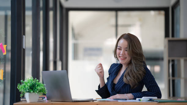 istock Young Asian woman celebrates winning or getting e-commerce shopping offer on computer laptop. Excited happy girl winner looking at notebook celebrating success. 1454110011
