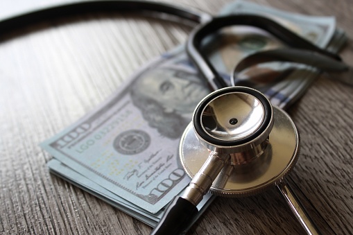 Stethoscope and money on wooden table. Healthcare, medical treatment cost and medicine concept.