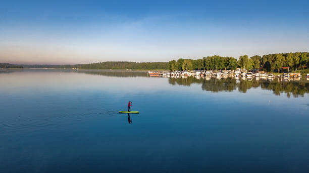 Woman paddling on SUP board on beautiful lake aerial drone view with reflections from above. Standing up paddle boarding adventure in early morning sunrise. Germany lake district Mecklenburg. Woman paddling on SUP board on beautiful lake aerial drone view with reflections from above. Standing up paddle boarding adventure in early morning sunrise. Germany lake district Mecklenburg. mecklenburg vorpommern stock pictures, royalty-free photos & images
