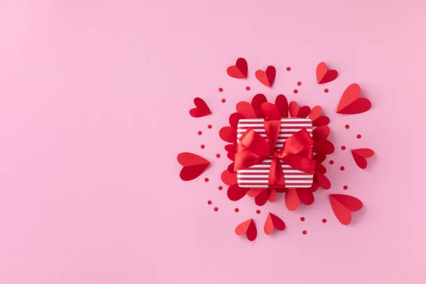 Gift or present box and paper hearts on pink table for Valentine day greeting card. Flat lay. stock photo