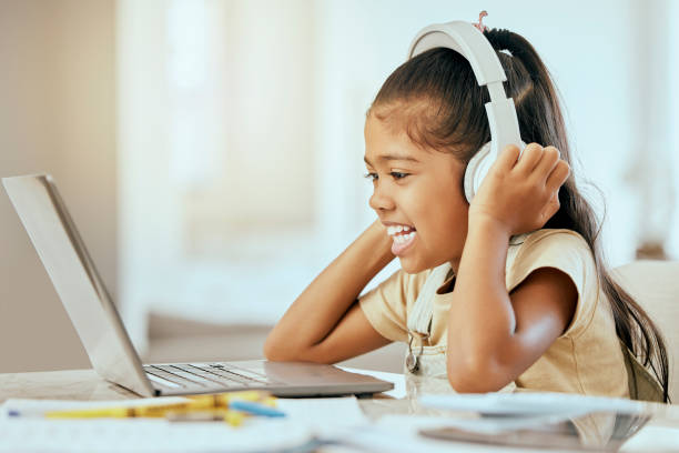 Girl, laptop and headphones with smile, music or video on desk in homeschool, learning and education, Child, computer and happy for podcast on internet, web or app by table in house for online class niña, computadora portátil y auriculares con sonrisa, música o video en el escritorio en la escuela en el hogar, aprendizaje y educación, niño, computadora y feliz para podcast en internet, web o aplicación por mesa en casa para clase en línea