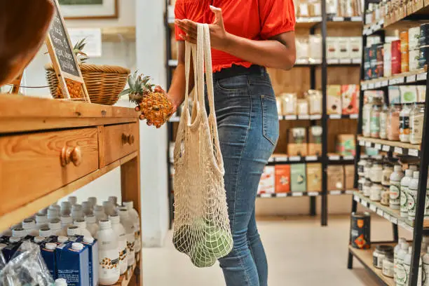 Woman, fruit shopping and pineapple in hand with ripe avo in bag at a supermarket grocery store looking for healthy food at discount price. Healthy, organic and natural fresh groceries for home lunch