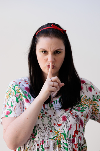 Woman with finger over mouth, requesting silence.