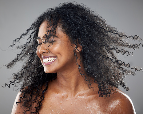 Beauty, wet and woman with a hair care and skincare treatment for wellness in the studio. Health, natural and happy model with a smile from Brazil moving her hair while isolated by a gray background.