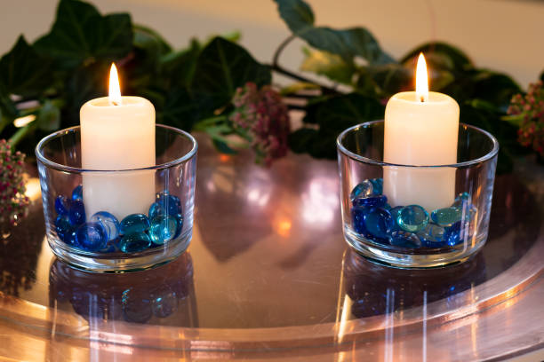 Lähikuva kahdesta valkoisesta kynttilästä, jotka on sytytetty pöydän lasiin ja kukkia taustalla kuvapankkikuva