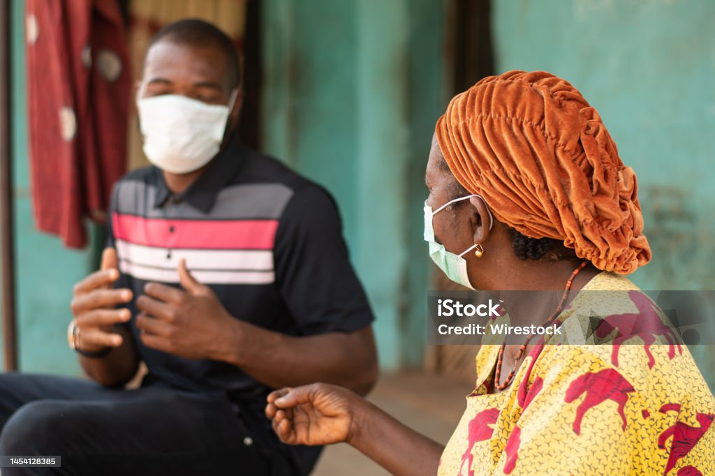 Elderly African woman and a young man wearing medical masks and chatting An elderly African woman and a young man wearing medical masks and chatting 18-19 Years Stock Photo
