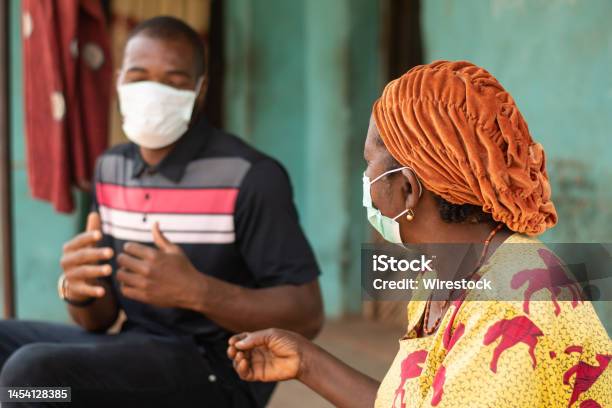 Elderly African Woman And A Young Man Wearing Medical Masks And Chatting Stock Photo - Download Image Now