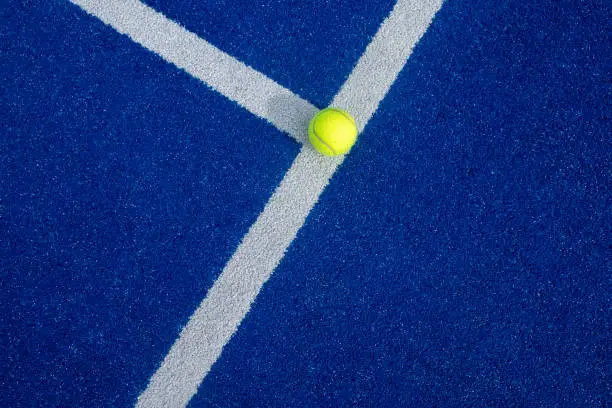 Close-up of a tennis ball on the white line of a paddle tennis court