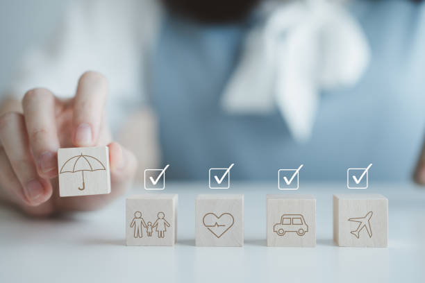 Insurance concept. Protection against a possible eventuality. Hand holding umbrella icon for security symbol and car, family, travel and health on wooden block with check mark. Life assurance concept.