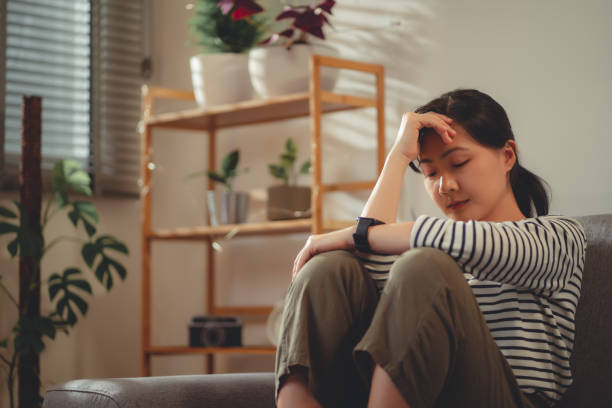 istock Asian woman feeling lonely thinking about problem sitting embracing knees on sofa. 1454131928
