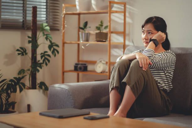 istock Asian woman feeling lonely thinking about problem sitting embracing knees on sofa. 1454132097