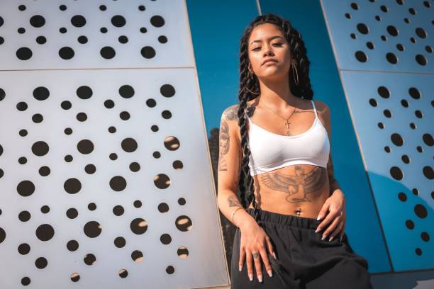istock Young Hispanic woman with long braids and tattoos posing under the sunlight 1454132169