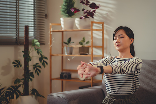 Asian woman suffering from hand pain massaging on wrist by hands sitting on sofa in living room at home.