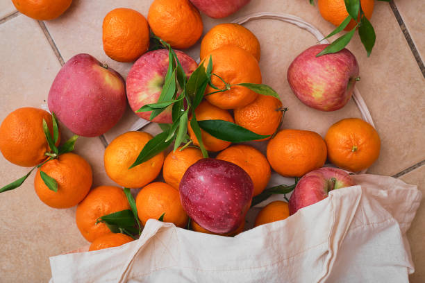 istock Red apples and tangerines in a reusable eco bag on a ceramic floor. Fruit delivery from farmers market, healthy food. Top view of juicy fruits. 1454133751