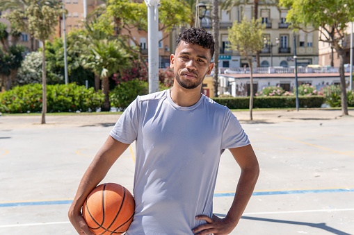 Portrait of a smiling young muslim man holding a basketball on a city court, urban sport concept, copy space