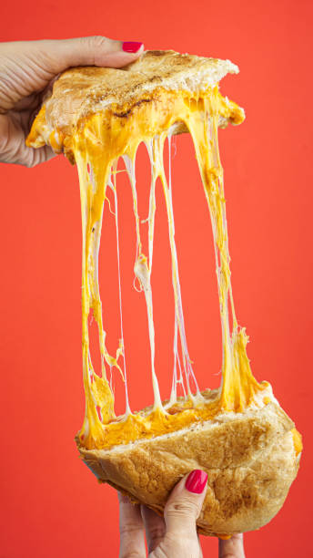 Vertical closeup of female hands holding cheese sandwich on a red background
