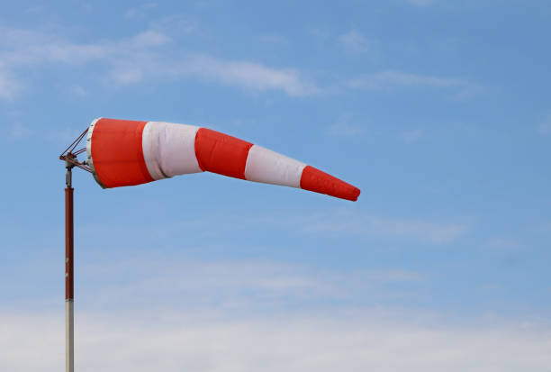 Red and white airport wind sock on blue sky with a few fluffy clouds blowing mostly straight out