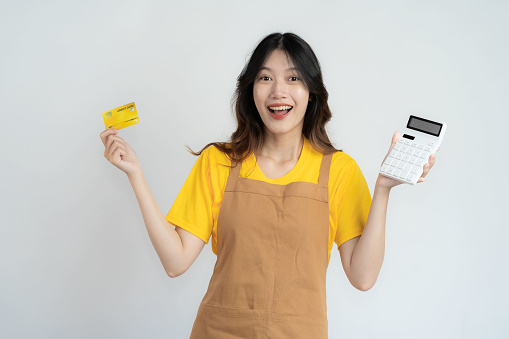 Pretty Asian woman holding credit card feeling proud and happy with shopping bags isolated on white background.