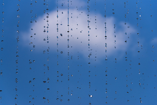 A selective focus of water dripping from a roof against blue sky