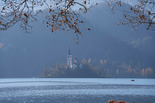 A scenic shot of a church surrounded by a lake, a forest, and mountains in Slovenia
