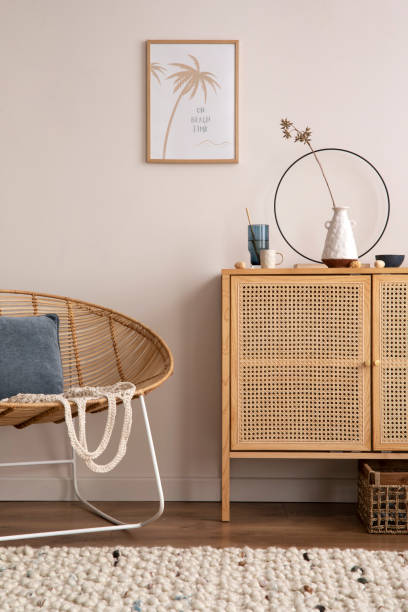 istock Cozy composition of living room interior with mock up poster frame, rattan comode, stylish armchair,  blue pillow, vase with dried flwers, beige wall, armchair and personal accessories. Home decor. Template. 1454144989