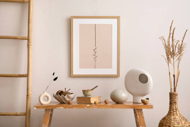 istock Simple composition of living room interior with mock up poster frame, beige wall, bench, leadder, vase with dried flowers, book and personal accessories. Home decor. Template. 1454145032