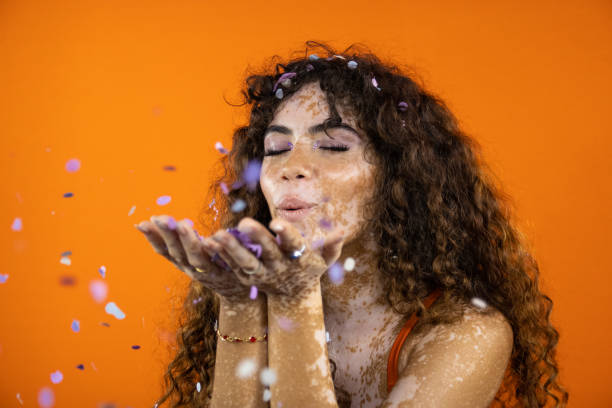 Woman blowing confetti on orange studio background stock photo