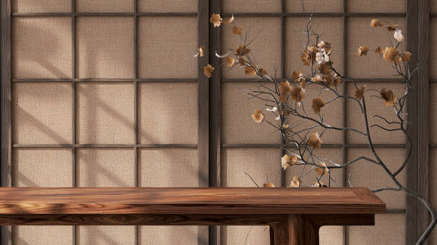 Wooden table top with dried tree branch and leaf in sunlight from window on traditional Japanese lattice frame wall with brown fabric sheet