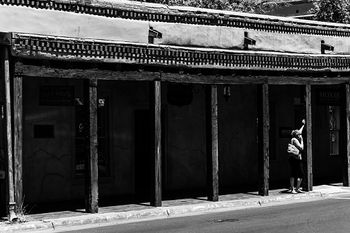 Santa Fe, United States – May 28, 2018: A grayscale of a tourist waiting for a cab outside an old building in Santa Fe, New Mexico