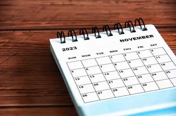 November 2023 white desk calendar on wooden table background.