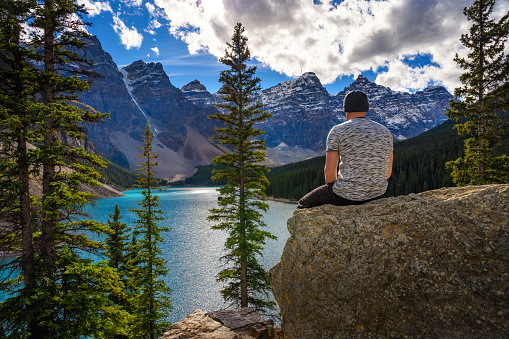 Hiker enjoying the view of Moraine lake in Banff National Park, Alberta, Canada, with snow-covered peaks of canadian Rocky Mountains in the background.