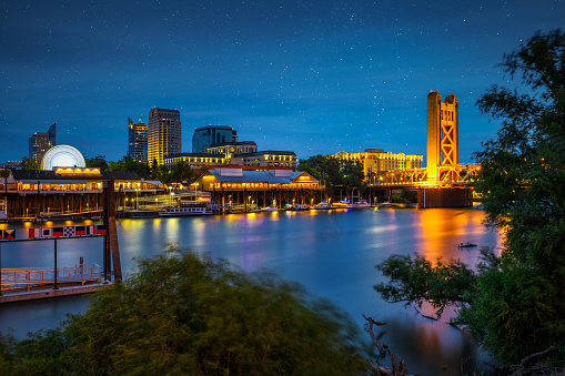 Gold Tower Bridge and Sacramento River in Sacramento, California, photographed from River Walk Park at night with stars in the sky.