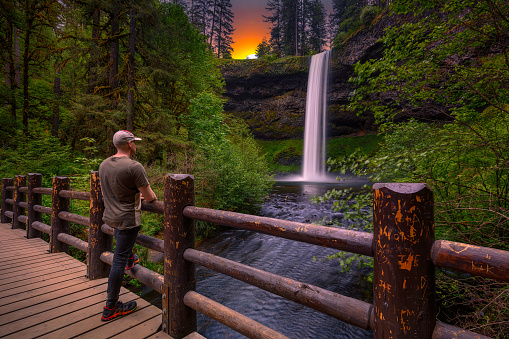 Tourist looking at the South Falls in Silver Falls State Park, Oregon. Photographed at sunset. Long exposure.