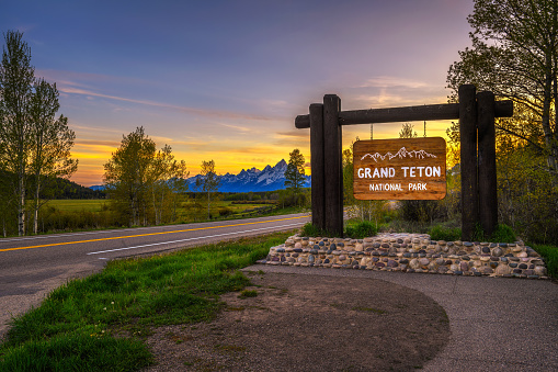 Welcome sign at the entrance to Grand Teton National Park in Wyoming, with Teton Mountain Range in the background. Photographed at sunset.