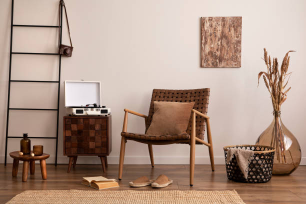 istock Creative composition of living room interior with mock up poster frame, comode, glass vase with dried flowers, armchair and personal accessories. Home decor. Template. 1454152709