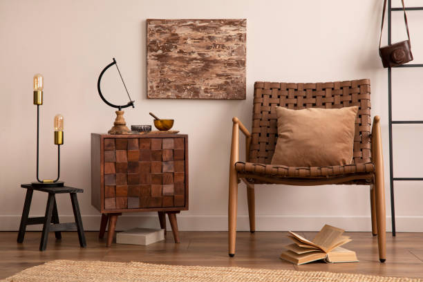 istock Warm and cozy interior of kitchen space with mock up poster frame, comode, armchair, brown pillow, book, boho rug, black stool, lamp and personal accessories. Beige wall. Template. 1454152723