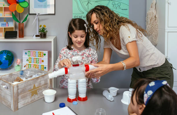 Teacher helping to girl make recycled toy robot with plastic packages stock photo